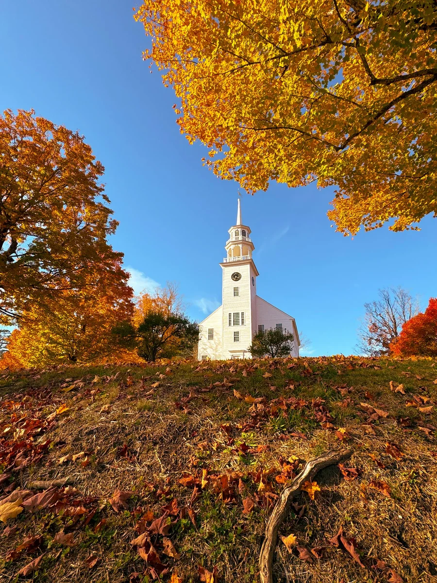Église blanche emblématique du Vermont entourée d'érables jaunes en automne
